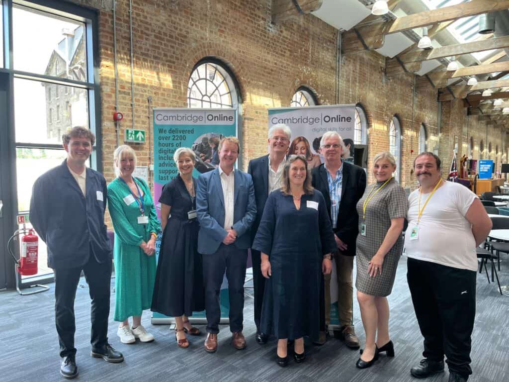 Bright, professional team gathering at a digital skills event with Cambridge Online banners, showcasing teamwork and conference environment in a stylish brick industrial venue.